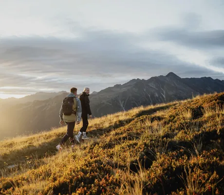 Paar wandert mit Rucksack auf einer herbstlichen Wiese auf dem Berg beim Wanderhotel Gassner