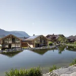 Alpzitt-Chalets am idyllischen Mühlenweiher mit Bergen im Hintergrund unter klarem Himmel