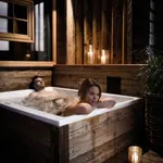 Zwei Personen entspannen in einem Holz-Whirlpool auf der Terrasse der Alpzitt-Chalets bei Kerzenlicht