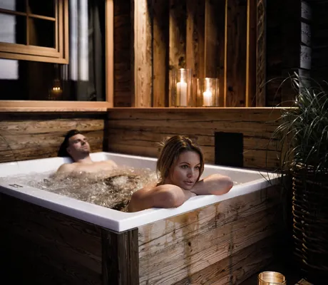 Zwei Personen entspannen in einem Holz-Whirlpool auf der Terrasse der Alpzitt-Chalets bei Kerzenlicht