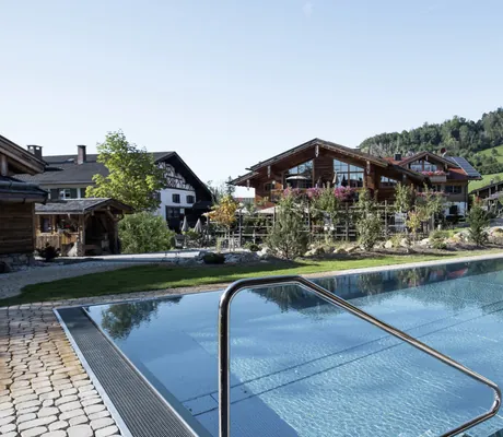 Außenpool umgeben von den Alpzitt-Chalets und bewaldeter Hügel im Hintergrund