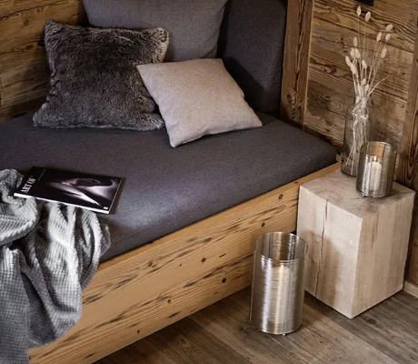 Sitzecke mit grauer Polsterung und Kissen, daneben ein kleiner Holztisch mit Glasvase und Kerzen in den Alpzitt-Chalets