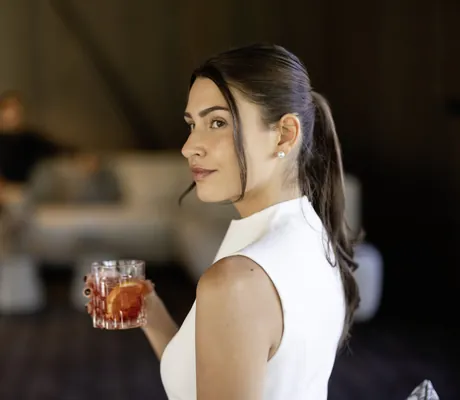 dunkelhaarige Frau in weißem Kleid trinkt einen Negroni in den Amonti Chalets