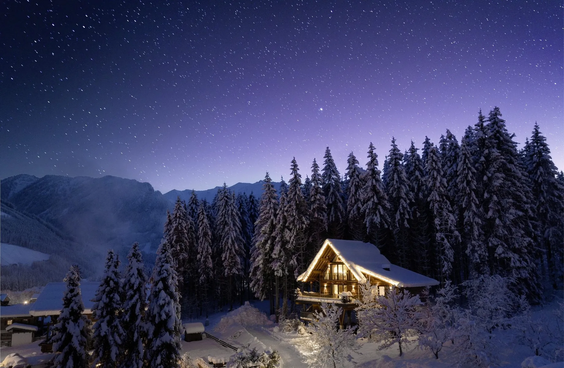 Blick auf das eingeschneite und mit Lichterketten beleuchtete Baumhaus des Hotel Gassner****Superior, darüber ein klarer Sternenhimmel