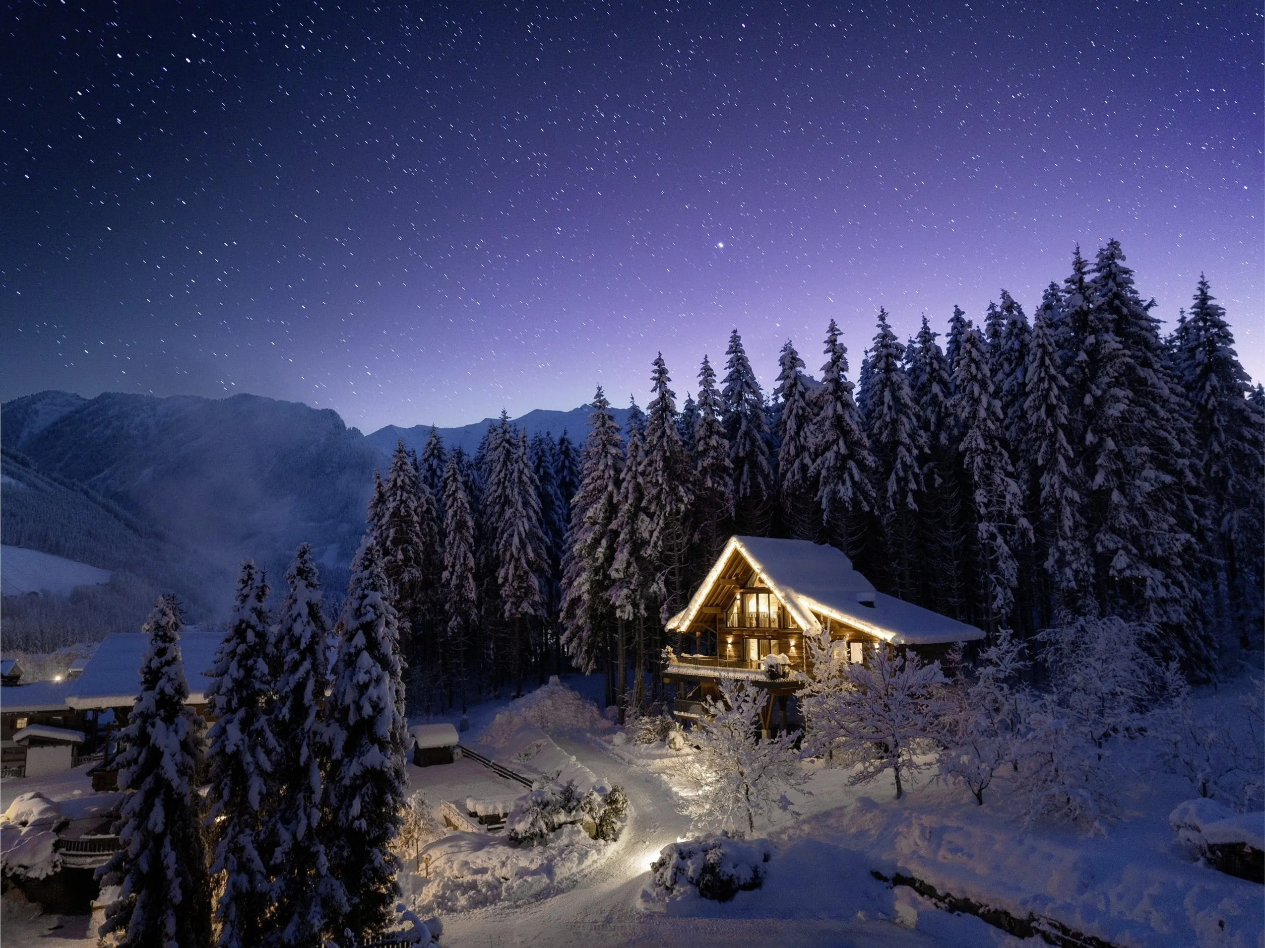Blick auf das eingeschneite und mit Lichterketten beleuchtete Baumhaus des Hotel Gassner****Superior, darüber ein klarer Sternenhimmel