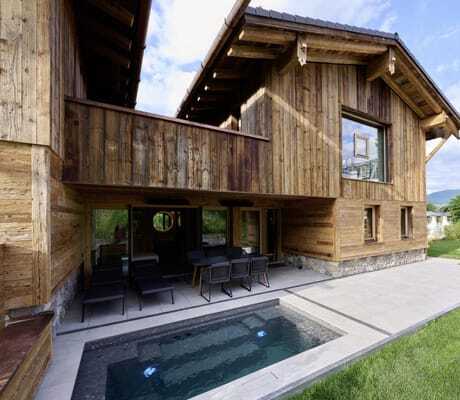 Außenansicht eines der Ziegelberg Chalets mit überdachter Terrasse, kleinem rechteckigem Pool und Bergblick unter blauem Himmel