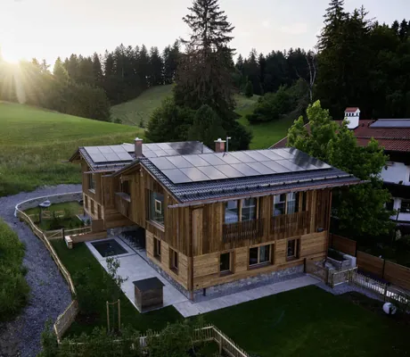 Blick auf die Ziegelberg Chalets mit Solarpaneelen auf dem Dach, umgeben von Wiesen und Bäumen bei Sonnenuntergang