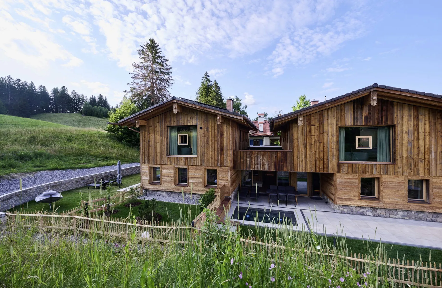Außenansicht der Ziegelberg Chalets mit mehreren Fenstern, Terrasse, Garten, umgeben von Wiese und Holzzaun unter blauem Himmel mit Wolken