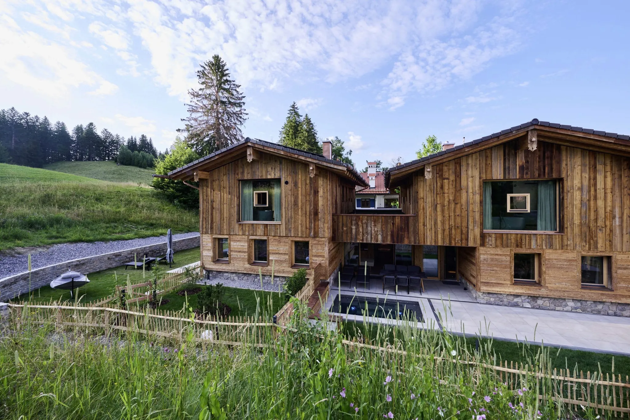 Außenansicht der Ziegelberg Chalets mit mehreren Fenstern, Terrasse, Garten, umgeben von Wiese und Holzzaun unter blauem Himmel mit Wolken