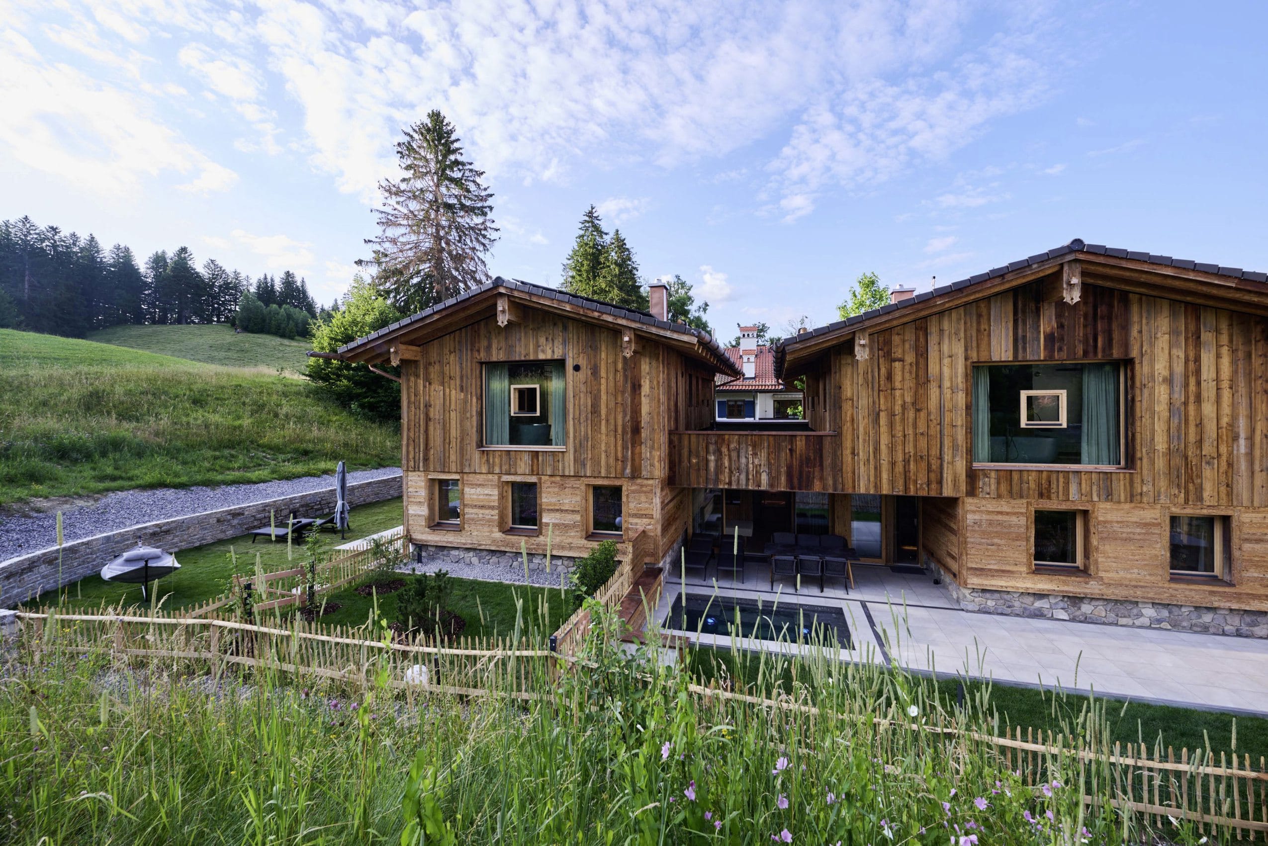 Außenansicht der Ziegelberg Chalets mit mehreren Fenstern, Terrasse, Garten, umgeben von Wiese und Holzzaun unter blauem Himmel mit Wolken
