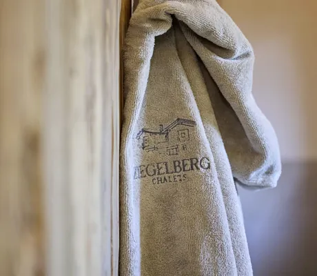 Nahaufnahme eines aufgehängten, beigefarbenen Bademantels mit dem Aufdruck Ziegelberg Chalets