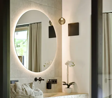 Runder Spiegel mit Beleuchtung über einem Steinwaschbecken mit schwarzem Wasserhahn und weißer Orchidee in einem Topf in den Ziegelberg Chalets