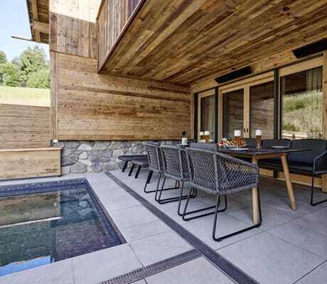 Terrasse der Ziegelberg Chalets mit großem, gedecktem Esstisch, Stühlen, Sitzbank und angrenzendem Pool