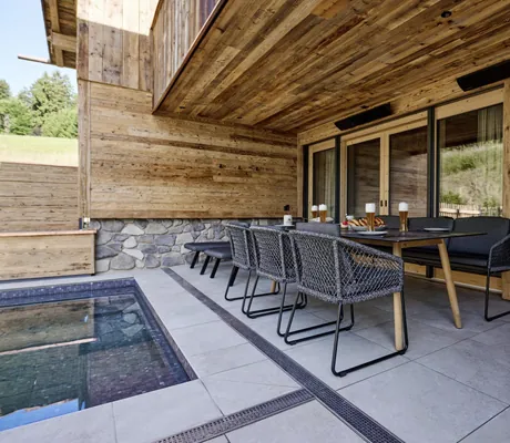 Terrasse der Ziegelberg Chalets mit großem, gedecktem Esstisch, Stühlen, Sitzbank und angrenzendem Pool