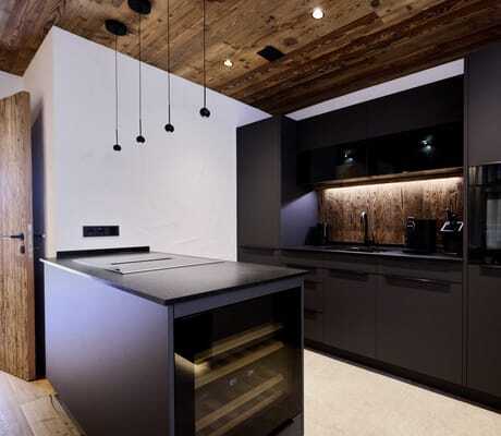 Moderne Küche in den Ziegelberg Chalets mit schwarzer Küchenzeile, integriertem Backofen, Holzdecke und Kücheninsel mit Weinkühlschrank