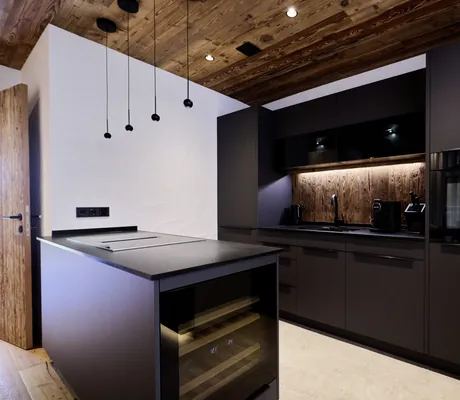Moderne Küche in den Ziegelberg Chalets mit schwarzer Küchenzeile, integriertem Backofen, Holzdecke und Kücheninsel mit Weinkühlschrank