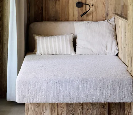 Gemütliche Sitzecke in den Ziegelberg Chalets mit weißem Polster, zwei Kissen, Holzverkleidung, grünem Wandbild und schwarzer Leselampe