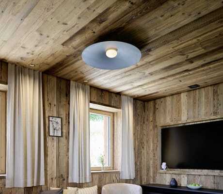 Wohnzimmer in den Ziegelberg Chalets mit hellbeigem Sofa, zwei runden schwarzen Beistelltischen auf hellem Teppich, Fenster mit weißen Vorhängen, wandmontierter Fernseher