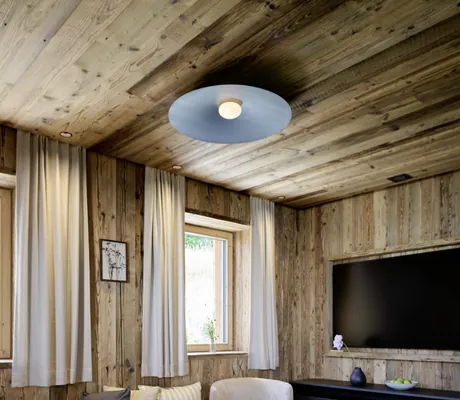 Wohnzimmer in den Ziegelberg Chalets mit hellbeigem Sofa, zwei runden schwarzen Beistelltischen auf hellem Teppich, Fenster mit weißen Vorhängen, wandmontierter Fernseher