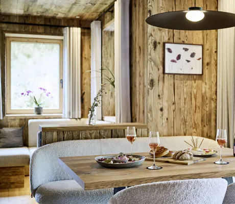 Gedeckter Holztisch in den Ziegelberg Chalets mit Champagner, Brot, Brezeln und Snacks, hängende Lampe und Fenster mit Blick ins Grüne