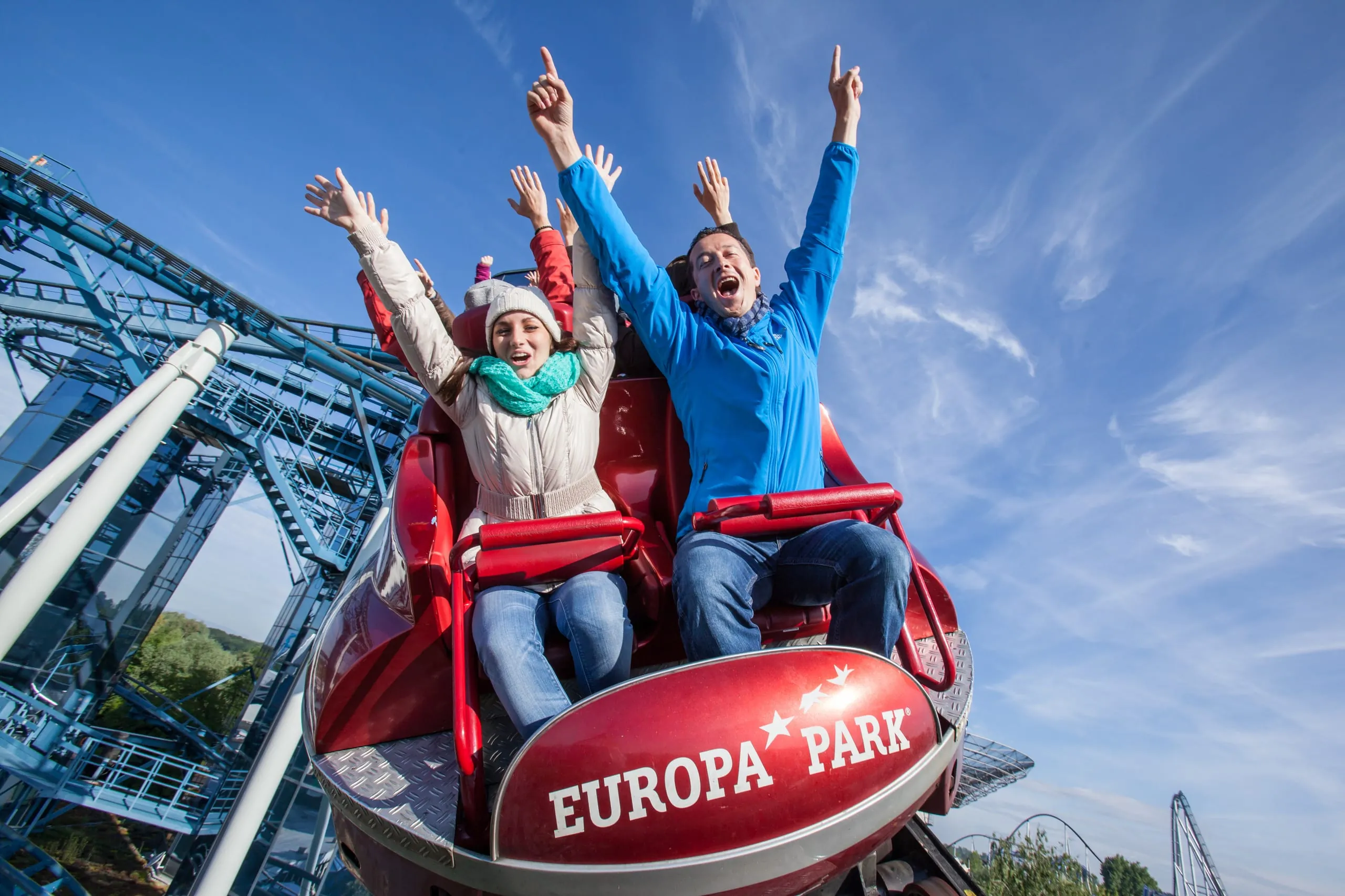 Jubelnde Menschen sitzen im Europa-Park in einem Achterbahn-Wagen und strecken die Hände in die Höhe