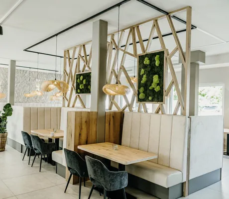 Moderner Restaurantbereich im Familienhotel Friedrichshof mit Holztischen, dunkelgrauen Stühlen, beigefarbenen Sitzbänken und offener Holztrennwand