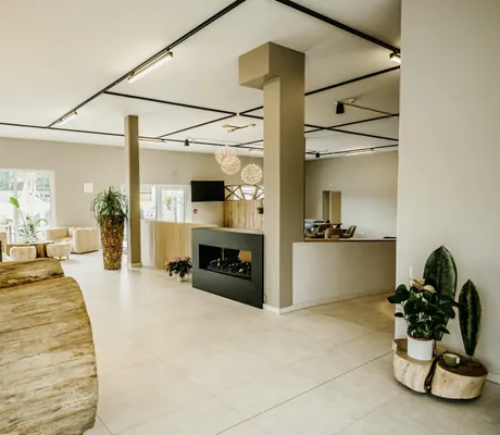 Rezeptionsbereich im Familienhotel Friedrichshof mit modernen Möbeln, großen Fenstern, Pflanzen und runden, hängenden Deckenleuchten