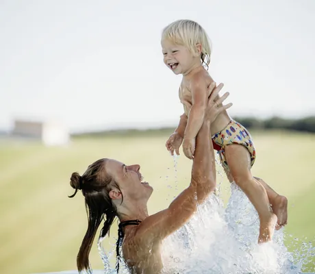 Frau wirft blondes Kleinkind im Wasser in die Luft im Outdoorpool des Hotel & Resort Landhaus zur Ohe