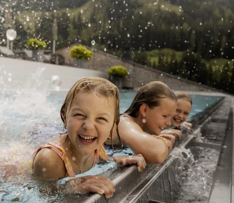 drei Kinder planschen am Beckenrand des Outdorpools im Tuxerhof