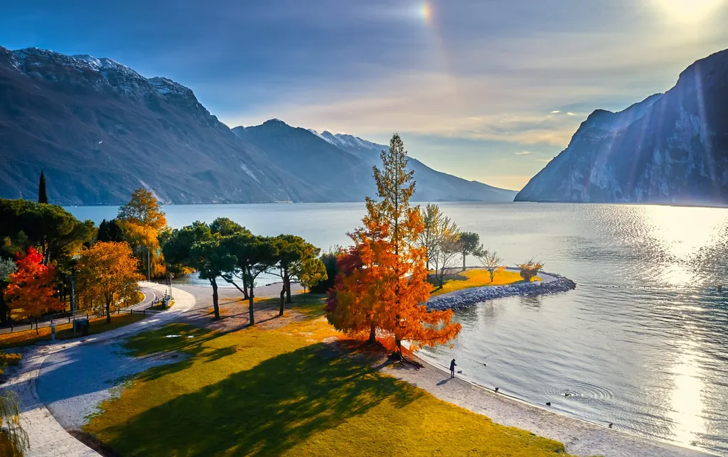 Blick von Riva del Garda über den Gardasee mit herbstlichen Bäumen im Vordergrund