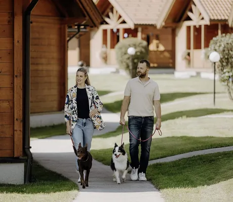 Zwei Personen laufen auf einem Weg durch das Chaletdorf ZellerSee, jede führt einen Hund an der Leine