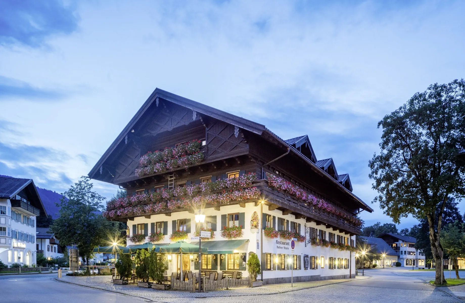 Außenansicht des Hundesporthotel Wolf am Abend mit Geranienkästen und grünen Sonnenschirmen