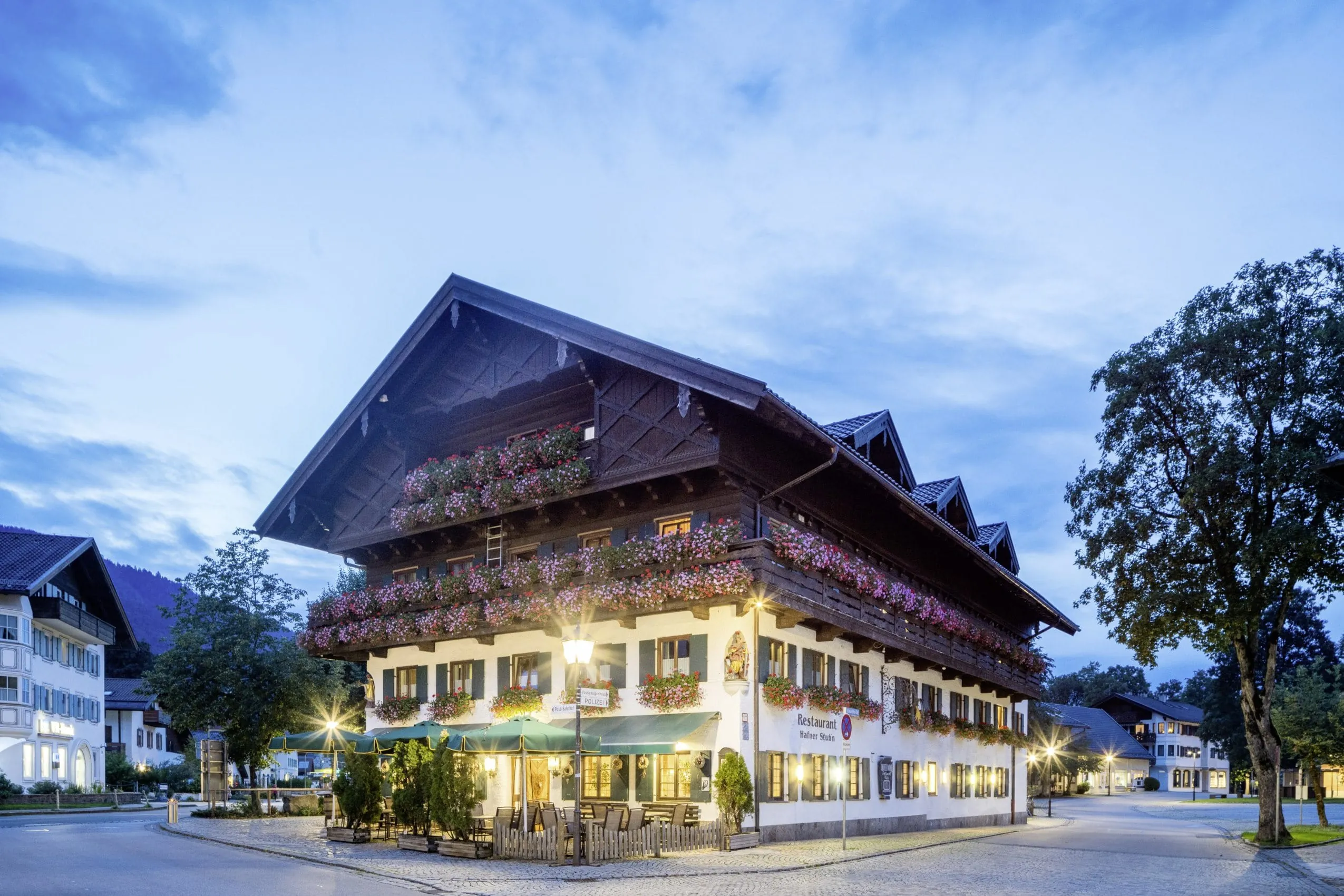 Außenansicht des Hundesporthotel Wolf am Abend mit Geranienkästen und grünen Sonnenschirmen