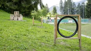 Hundespielplatz in der Nähe des Hotel Mischun mit zwei Hindernissen, im Hintergrund Bäume und Berge