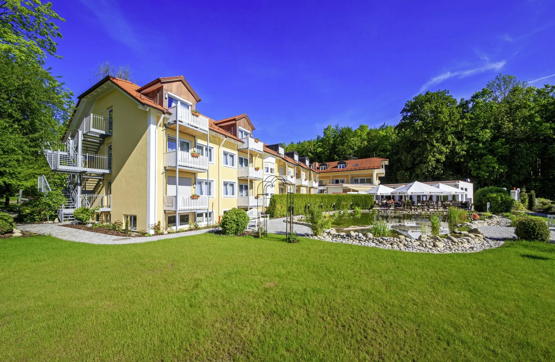 Naturteich vor gelber Fassade mit weißen Balkonen des Ringhotel Sonneck
