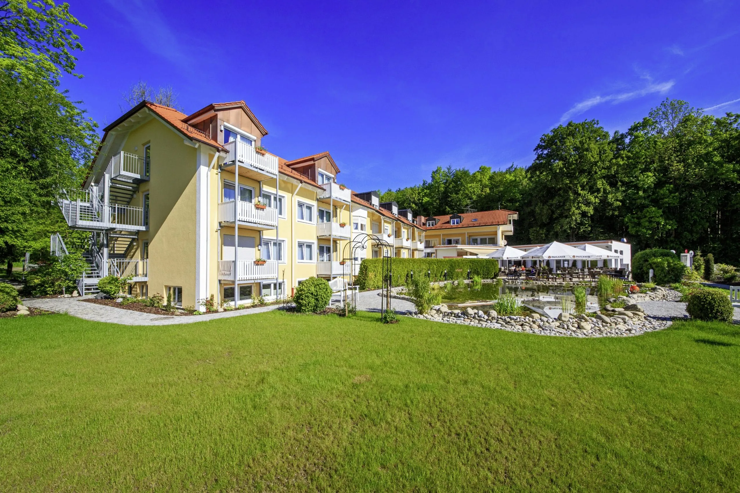 Naturteich vor gelber Fassade mit weißen Balkonen des Ringhotel Sonneck