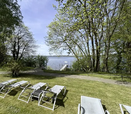 Liegewiese am See mit Holzsteg und grauen Sonnenliegen im Seehotel Heidehof