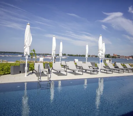 Liegen und Sonnenschirme am Outdoorpool des Maremüritz Yachthafen Resort mit Blick auf den See und den Ort
