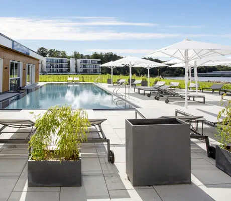 Outdoorpool im Maremüritz Yachthafen Resort vor dem Wellnessbereich mit Liegen und Sonnenschirmen