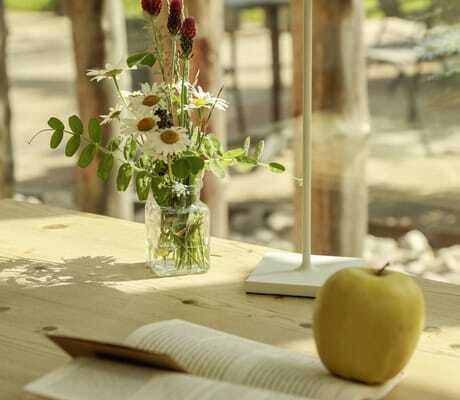 Holztisch mit Blumen, Lampe, Apfel und einem aufgeschlagenen Buch