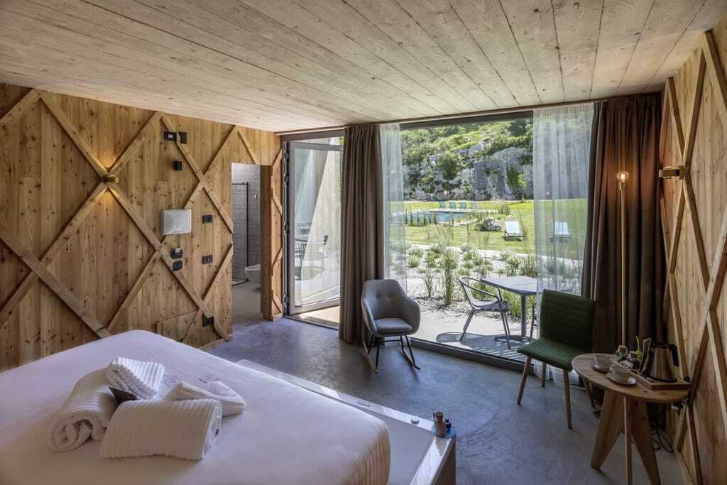Zimmer komplett aus Holz und bodentiefen Fenstern, durch die man auf den Outdoorpool im Agritur La Dolce Mela sieht