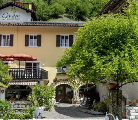 Blick auf den Eingang des Good Life Hotel Garden mit viel Grün und beschirmter Terrasse
