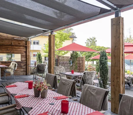 Überdachte Terrasse im Tagungshotel schiller‘s mit eingedeckten Tischen und roten Farbakzenten