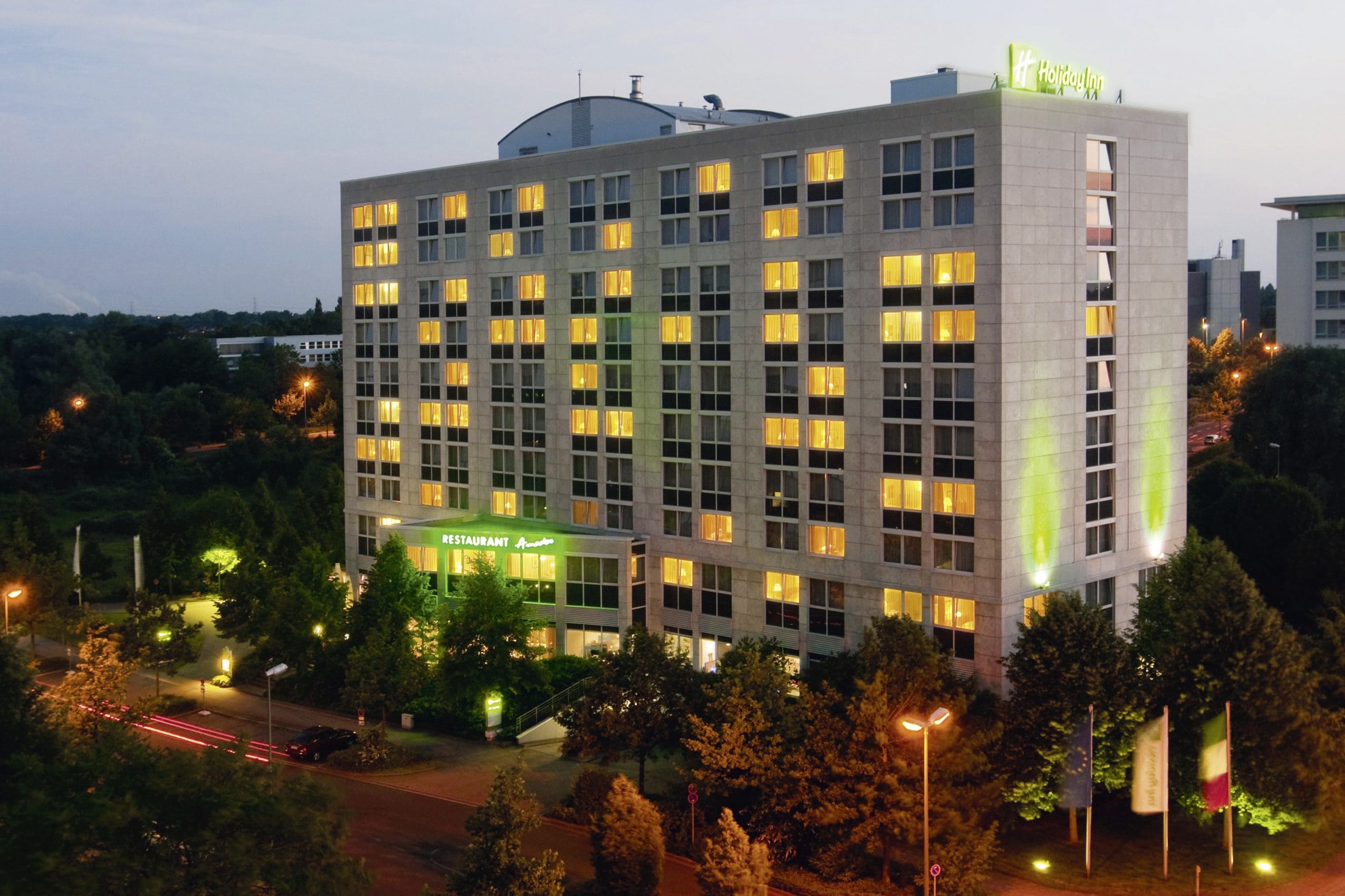 Außenansicht des Holiday Inn Neuss im Abendlicht mit beleuchtetem Logo
