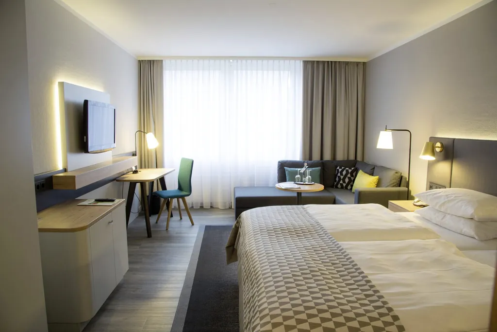 Zimmer im Holiday Inn Neuss mit gemustertem Bettüberwurf und grauem Ecksofa