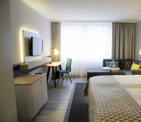Zimmer im Holiday Inn Neuss mit gemustertem Bettüberwurf und grauem Ecksofa
