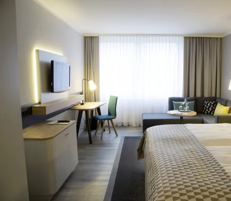 Zimmer im Holiday Inn Neuss mit gemustertem Bettüberwurf und grauem Ecksofa