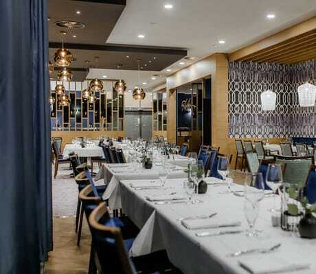 langer eingedeckter Tisch im Restaurant des Hotel am Vitalpark mit blauen Stühlen und kupferfarbenen Lampen