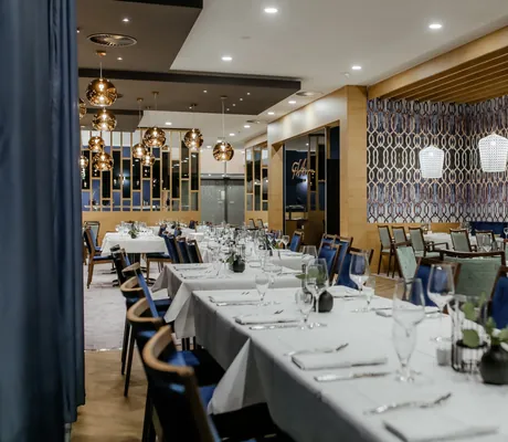 langer eingedeckter Tisch im Restaurant des Hotel am Vitalpark mit blauen Stühlen und kupferfarbenen Lampen