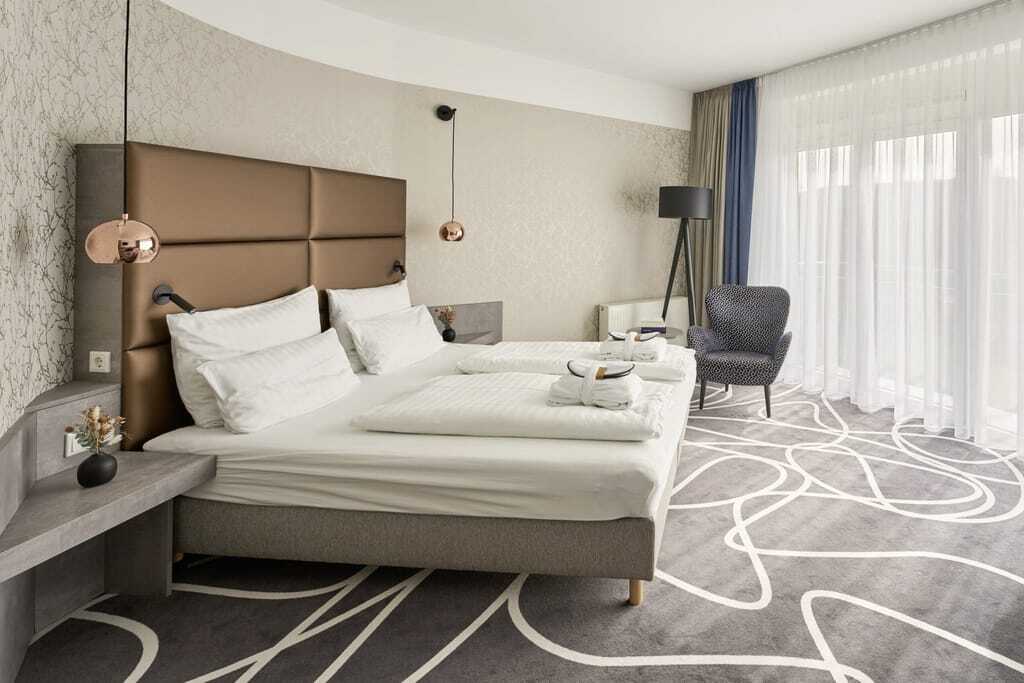 Zimmer im Hotel am Vitalpark mit weißem Schlingenmuster im grauen Teppich und kupferfarbenen Lampen
